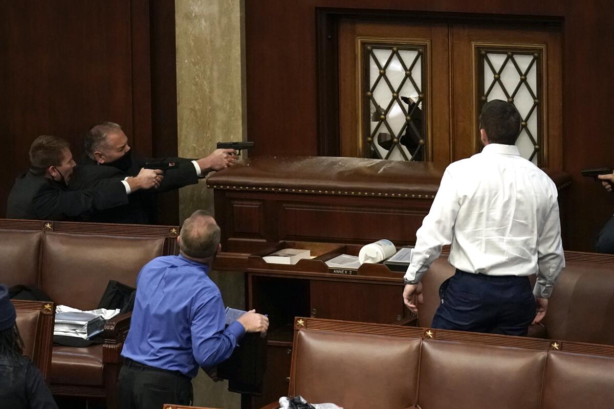 Two police officers have guns drawn as they watch the doors of the House chamber, blocked by a bookcase.